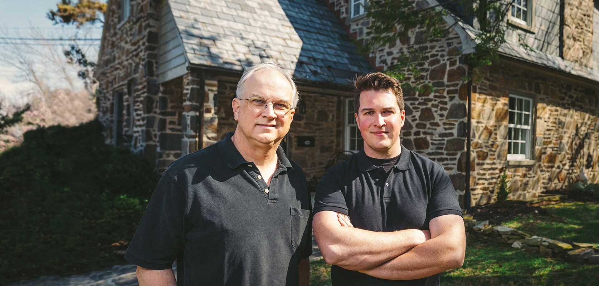 Frank & Sam Taciak of C.A. Taciak & Sons standing in front of an english style stone house