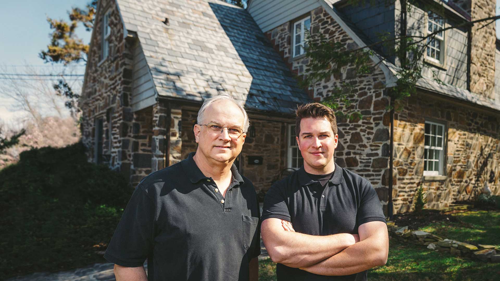 Frank & Sam Taciak of C.A. Taciak & Sons standing in front of an english style stone house